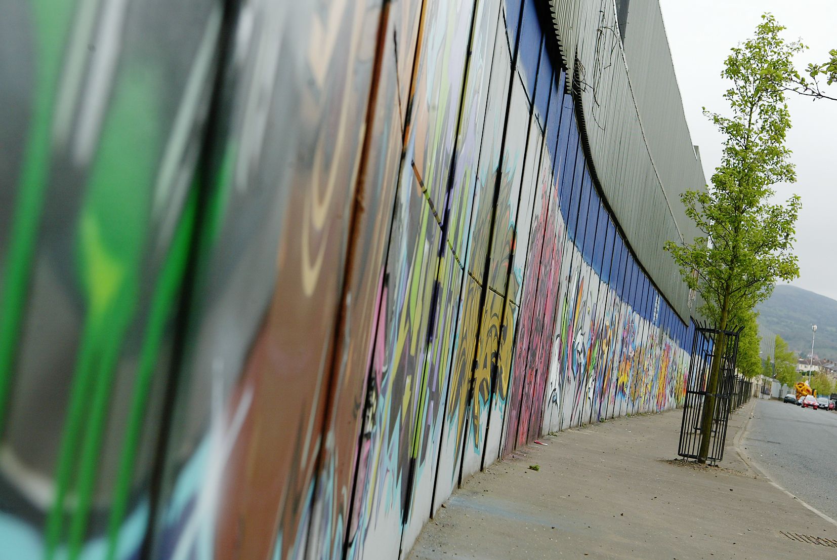 A section of the Belfast peace wall — concrete and steel layered with murals, graffiti and decades of colour. Photograph by Thomas McMullan.